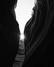 This classic black and white photograph captures a sunset illuminating sandstone cliffs in a canyon from a dramatic low-angle