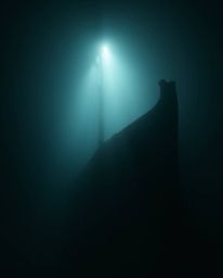 A stunning underwater shipwreck scene captured with mesmerizing chiaroscuro lighting. The image evokes a soft, dreamy atmosph