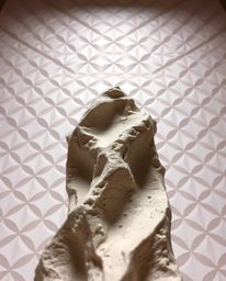 This artwork features a low-angle, dramatic sculptural clay piece with textured, modeled shapes, inviting the viewer to look 