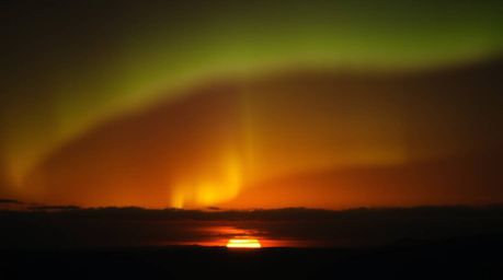 A stunning fine art photograph captures the intense drama of the Northern Lights emerging over a vibrant sunset sky.  Warm, s