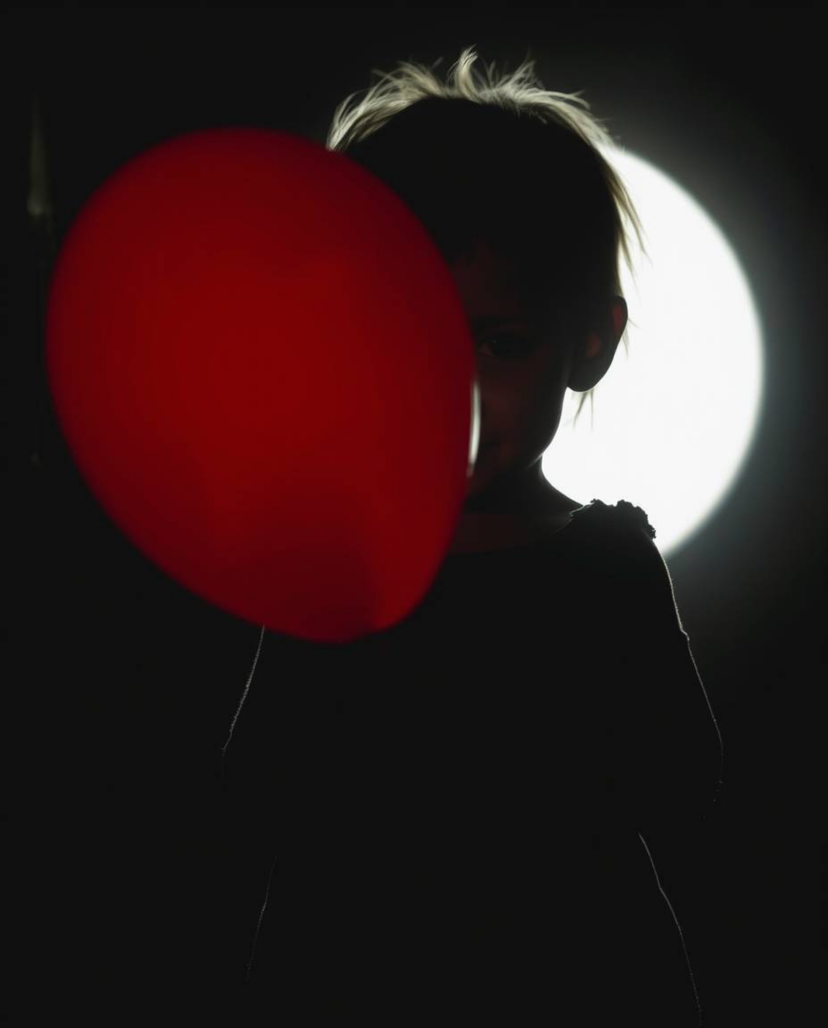 A captivating image of a child with delicate features holding a red balloon, silhouetted against a bright light source. The d