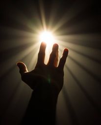 A captivating fine art photograph depicts a hand extending towards a radiant light source emerging from darkness.  The image 