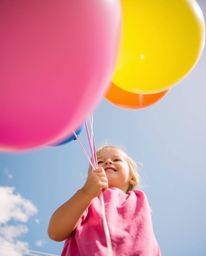 A captivating low-angle shot captures a child joyfully holding a vibrant balloon.  The image is bursting with bright colors a