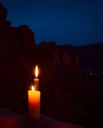 Warm candlelight illuminates sandstone cliffs at sunset, creating a scene with a sophisticated and elegant aesthetic. The lan