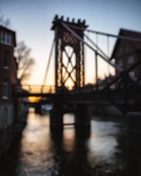 A captivating digital sketch portrays an old wooden bridge over a river, set against a beautiful sunset. The scene is illumin