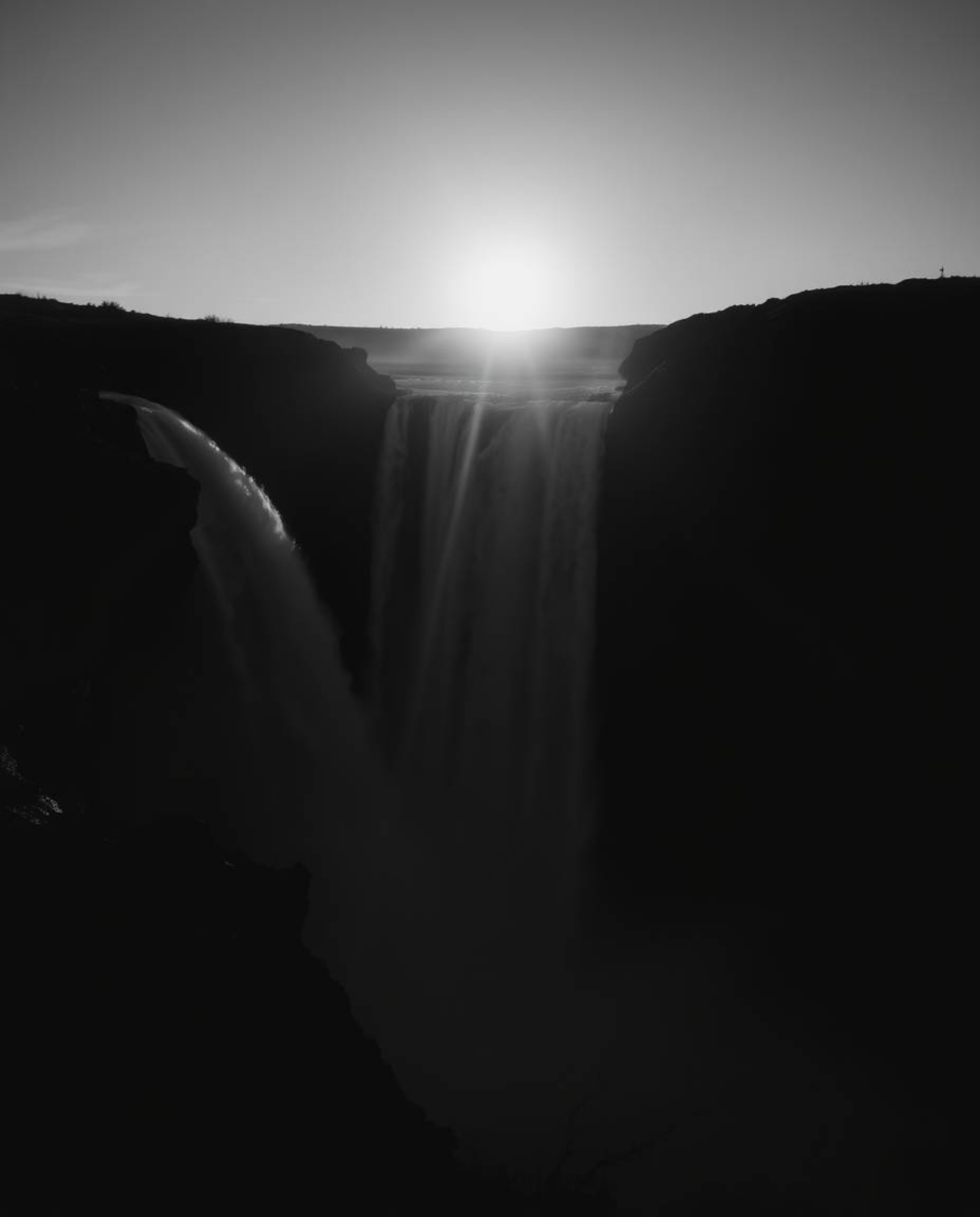 From a high-angle perspective with high contrast and low-key lighting, this image captures a sun setting behind a dramatic wa
