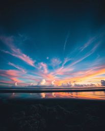 A striking high-angle perspective captures a colorful sky over a coral reef at low tide. The image employs high-contrast and 