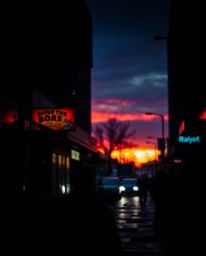 This piece of candid street photography captures an eerie atmosphere as snowflakes fall during a vibrant sunset in an urban s