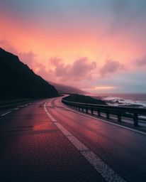 This high dynamic range photograph captures a wet, rainy sunset scene over a winding coastal highway from a dramatic low-angl
