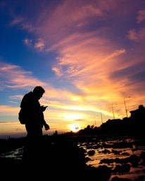 This artwork captures a coral reef at low tide under a colorful sky through the lens of silhouetted candid street photography