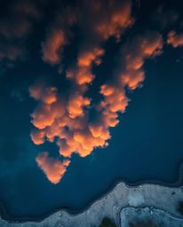 An overhead bird's eye view digital photograph captures a mountain lake reflecting fiery clouds. This top-down perspective pr