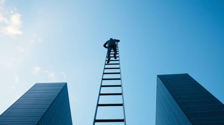 A stunning fine art photograph depicts a businessperson ascending a transparent ladder into a vibrant blue sky above towering