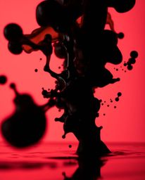 A captivating macro photograph reveals a mesmerizing display of jet-black ink splashing into water against a vibrant backdrop