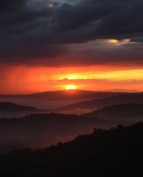 A warm intense dramatic sunset over misty Tuscan hills, with stormy skies creating high tension, all depicted in a vibrant re