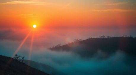 A surreal and dreamlike landscape featuring fog-covered hills bathed in the warm glow of a sunset, complete with a vibrant le