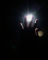 A captivating photograph showcasing a hand reaching from the darkness towards a source of light. The hand is in sharp focus, 