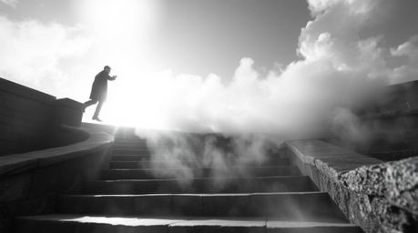 A striking black and white macro photograph capturing a lone figure ascending a stone staircase into a radiant beam of divine