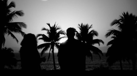 Capture the essence of a tranquil tropical evening with this stunning black and white image. Silhouetted figures stand agains