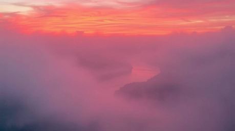 A captivating close-up reveals a winding river bathed in the warm glow of a dramatic orange-pink sunset.  Thick fog shrouds t