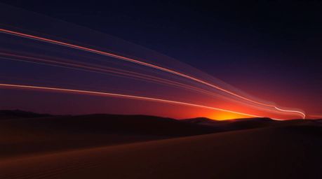 Stunning long exposure photograph capturing a vibrant sunset over dramatic desert dunes.  The image features intense lighting