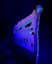 Discover a breathtaking underwater scene of a graceful shipwreck illuminated in deep ultraviolet light.  Vivid purples and st