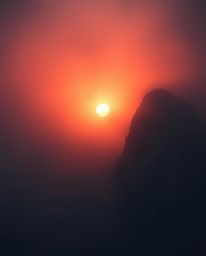 Venture into a dark and eerie depiction of a sunset from a high alpine peak, where the view is obscured by thick fog. This cr