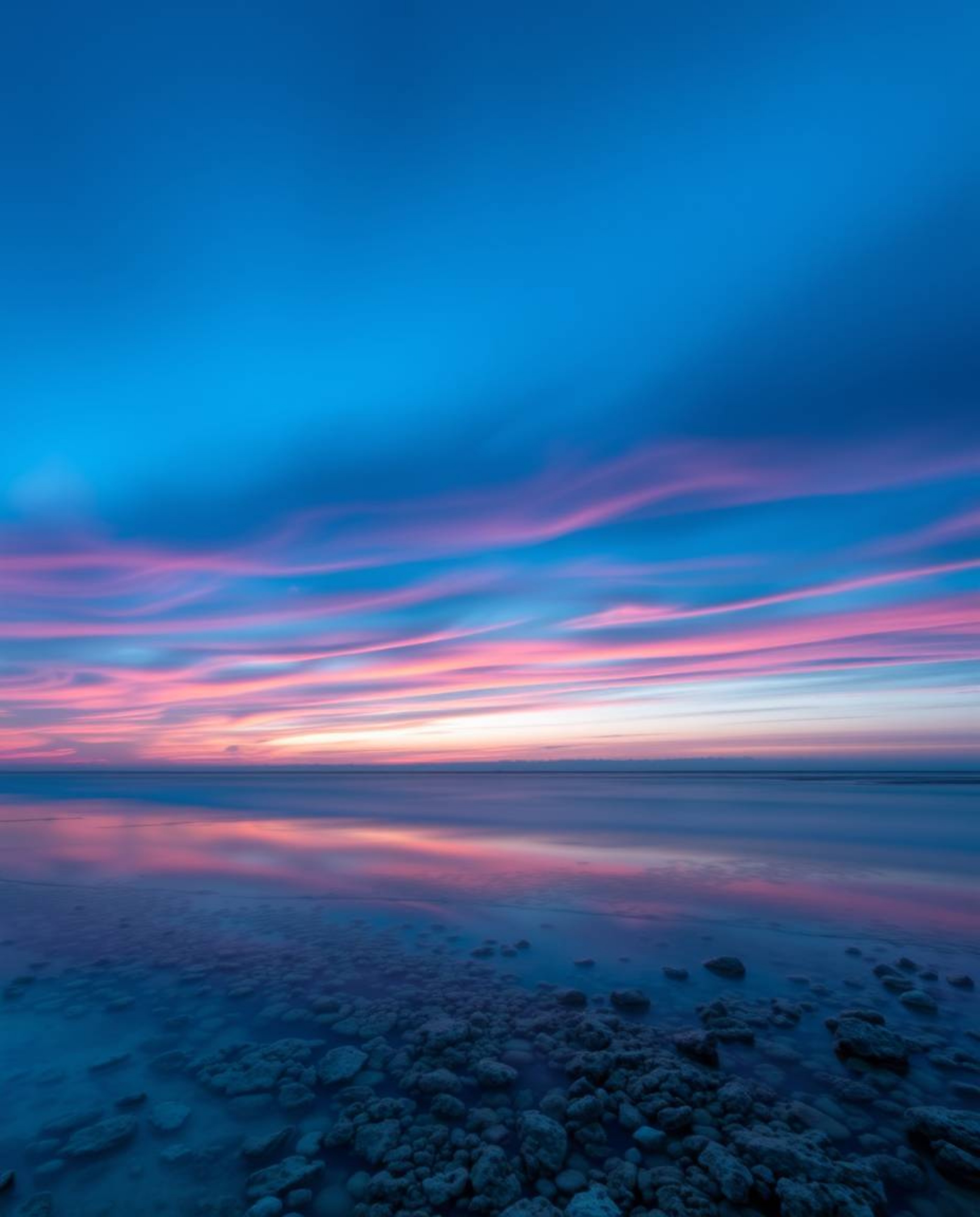 A graceful and elegant long exposure photograph captures a colorful sky over a coral reef at low tide. The image is distingui