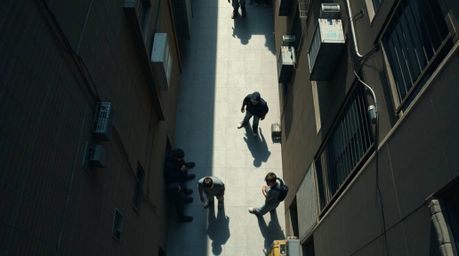 A captivating top-down shot reveals a grungy city alley teeming with rebellious teens.  Harsh overhead lighting casts dramati