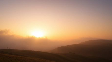 Experience a dramatic and captivating landscape featuring fog-covered hills bathed in the warm, natural earth tones of brown 