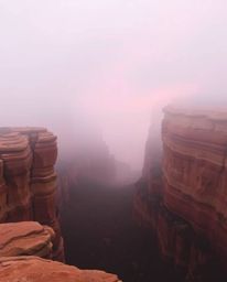 Sandstone cliffs at sunset are obscured by a thick, atmospheric fog, creating a scene of mysterious beauty. Despite the low v