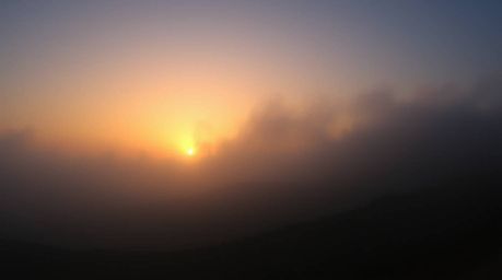Experience the breathtaking beauty of fog-covered hills at sunset. This dramatic low-angle shot captures the golden light bre