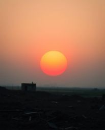 A striking close-up capturing a sunrise over a desolate, war-torn landscape. The image showcases a compelling contrast betwee