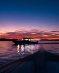 Long exposure photograph of a boat on a lake at sunset, iridescent colors create shimmering reflections and capture motion, l