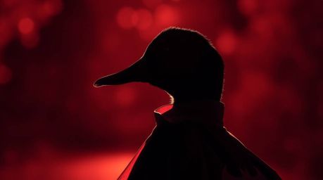 This image features a striking close-up shot of a silhouetted duck dressed in a superhero costume.  Backlit with surreal infr