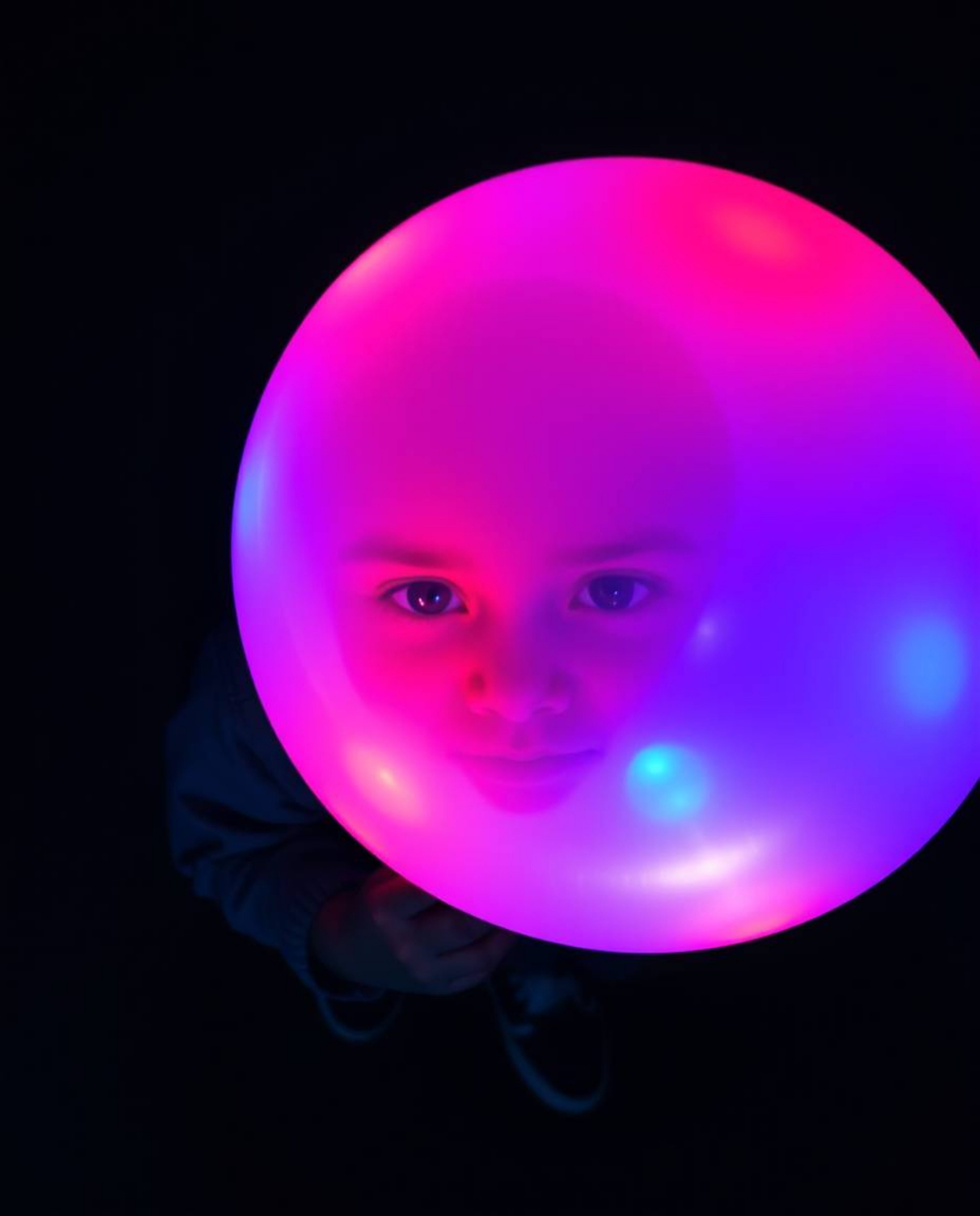 A captivating overhead shot depicts a child with dark skin joyfully holding a bioluminescent balloon, radiating vibrant, glow