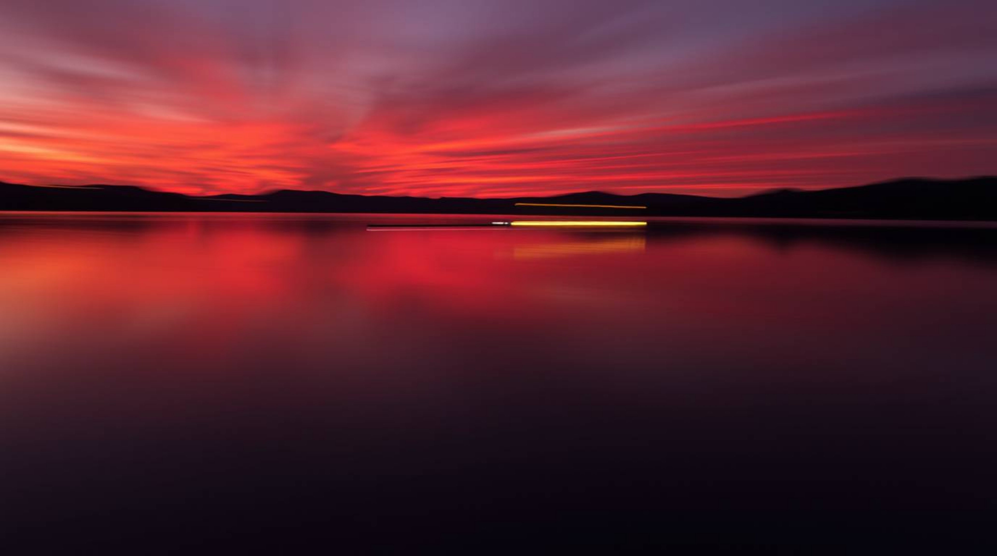 Capture the serene beauty of a lake reflecting a vibrant sunset. This long exposure photograph showcases warm reds, oranges, 