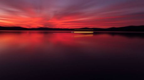 Capture the serene beauty of a lake reflecting a vibrant sunset. This long exposure photograph showcases warm reds, oranges, 