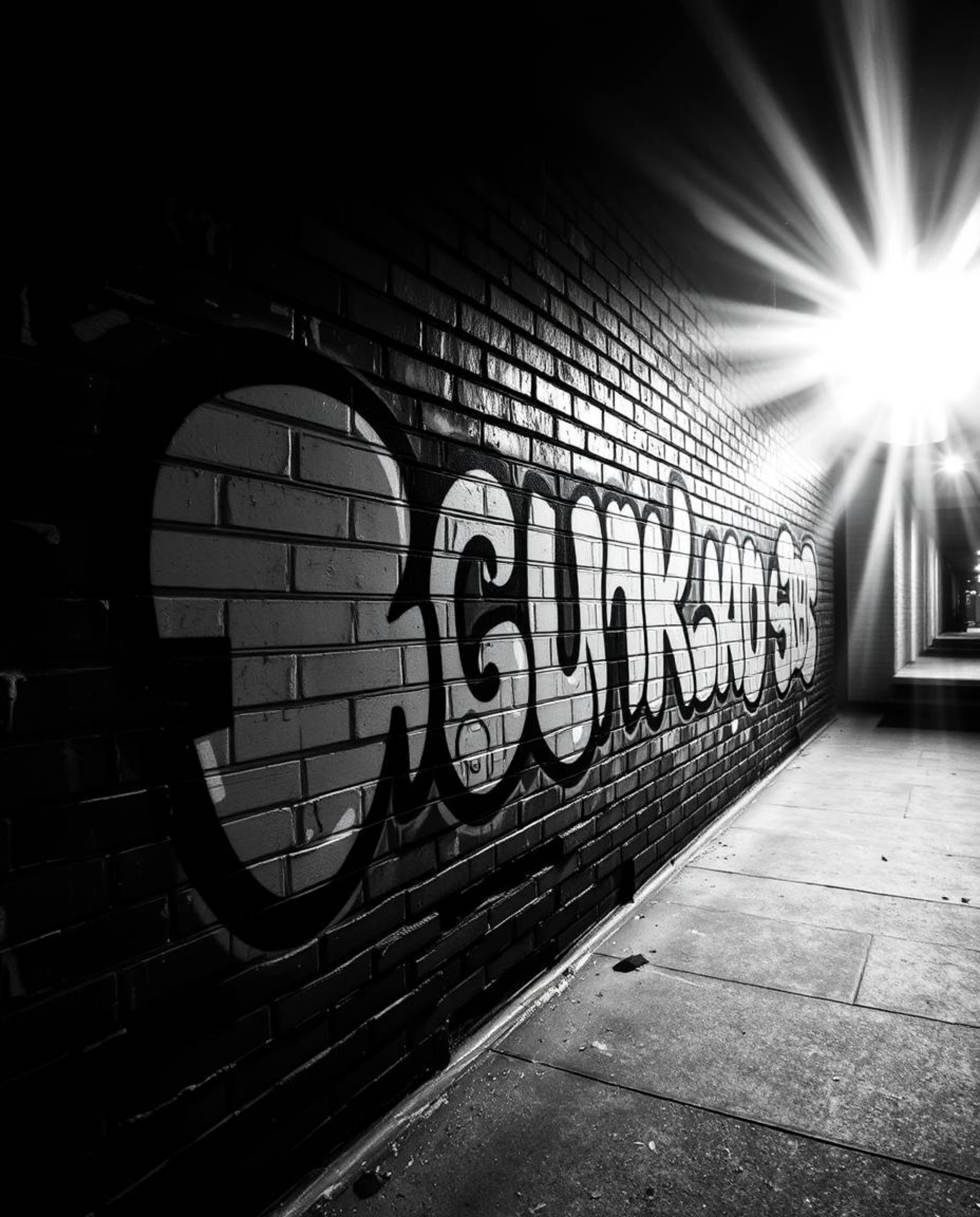 A classic black and white photograph capturing the energy of graffiti-style colorful splashes against a brick wall. The image