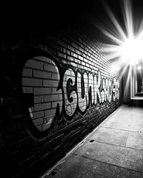 A classic black and white photograph capturing the energy of graffiti-style colorful splashes against a brick wall. The image