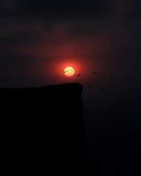 Unusual and original fine art photography captures a sunset over a coastal cliff with soaring birds. The piece is characteriz