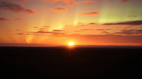 Experience the magic of the Northern Lights dancing across a breathtaking sunset sky. This captivating scene blends warm terr