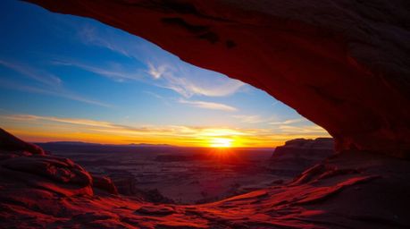 A captivating photograph capturing an ethereal desert sunset framed by a natural rock arch.  The image showcases vibrant, com