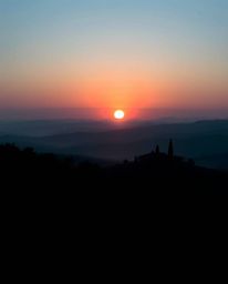 Capture the serene beauty of a sunset over misty Tuscan hills, viewed from a striking low-angle perspective. This image featu