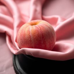 A captivating high-angle close-up showcasing a soft, blushing pink peach resting on silky pastel pink fabric. The image boast