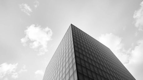 A captivating black and white image presents a modern glass building seamlessly merging into a sky adorned with soft clouds, 