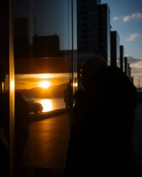 A high-contrast, low-key candid street photograph capturing spontaneous moments. This image features the reflection of a suns