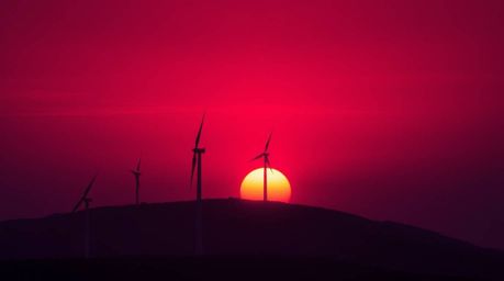 A captivating high-resolution stock photo showcasing a vibrant sunset cascading behind a row of wind turbines perched atop a 