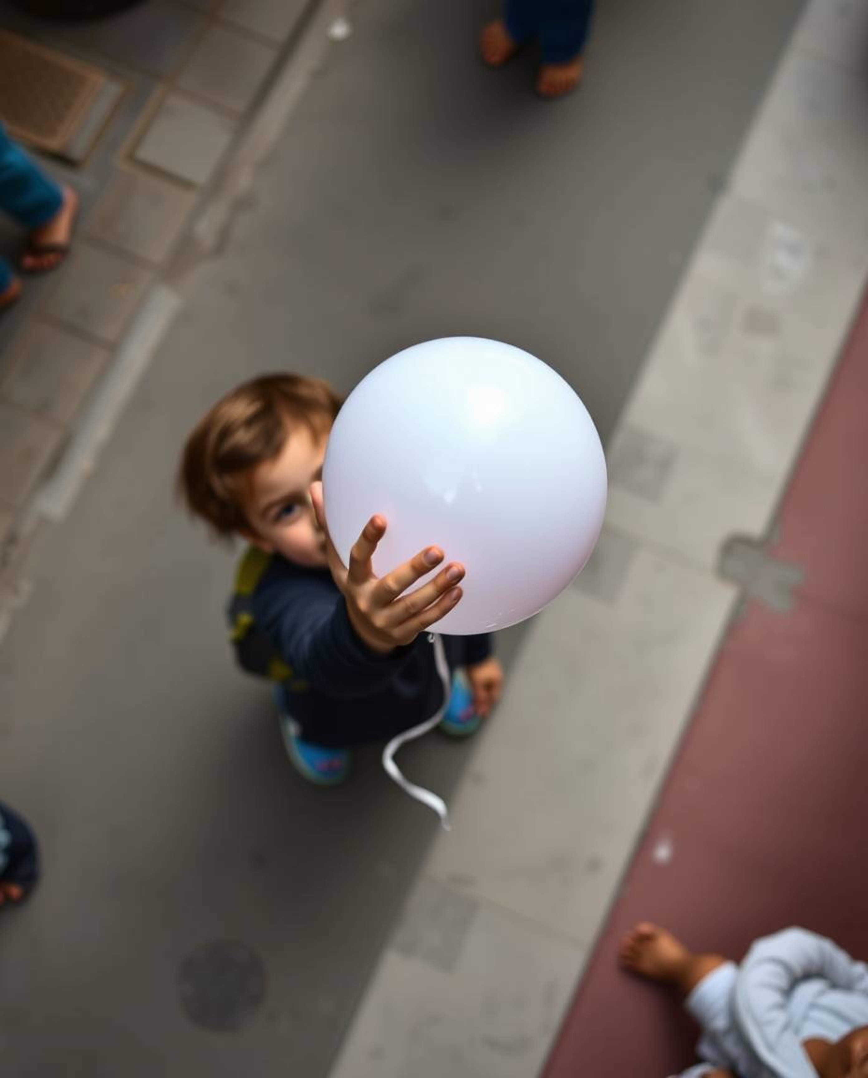 Capturing the essence of urban life, this candid street photograph presents a child holding a balloon from an overhead bird's