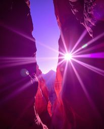 A dramatic scene unfolds as deep ultraviolet hues accentuate sandstone cliffs illuminated by a canyon sunset. A bright lens f