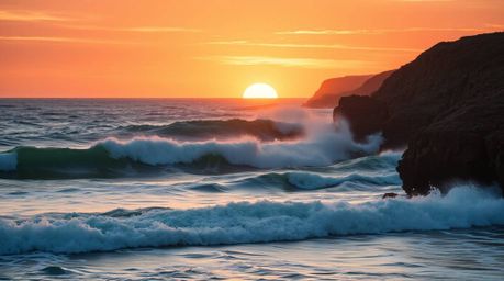 Witness the breathtaking scene of waves crashing against dramatic cliffs under a blazing sunset sky. The interplay of warm te